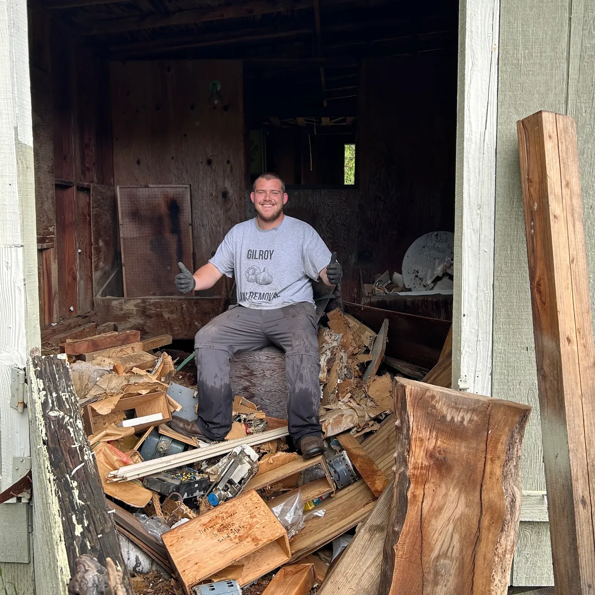 Gilroy Junk Removal crew member on a pile of wood and debris inside an old outbuilding before cleanout