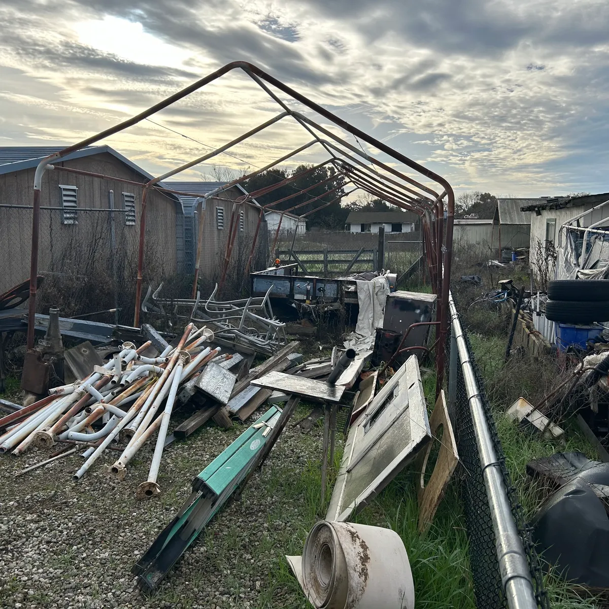 Outdoor property lot piled with scrap metal, lumber, and old equipment before haul-off